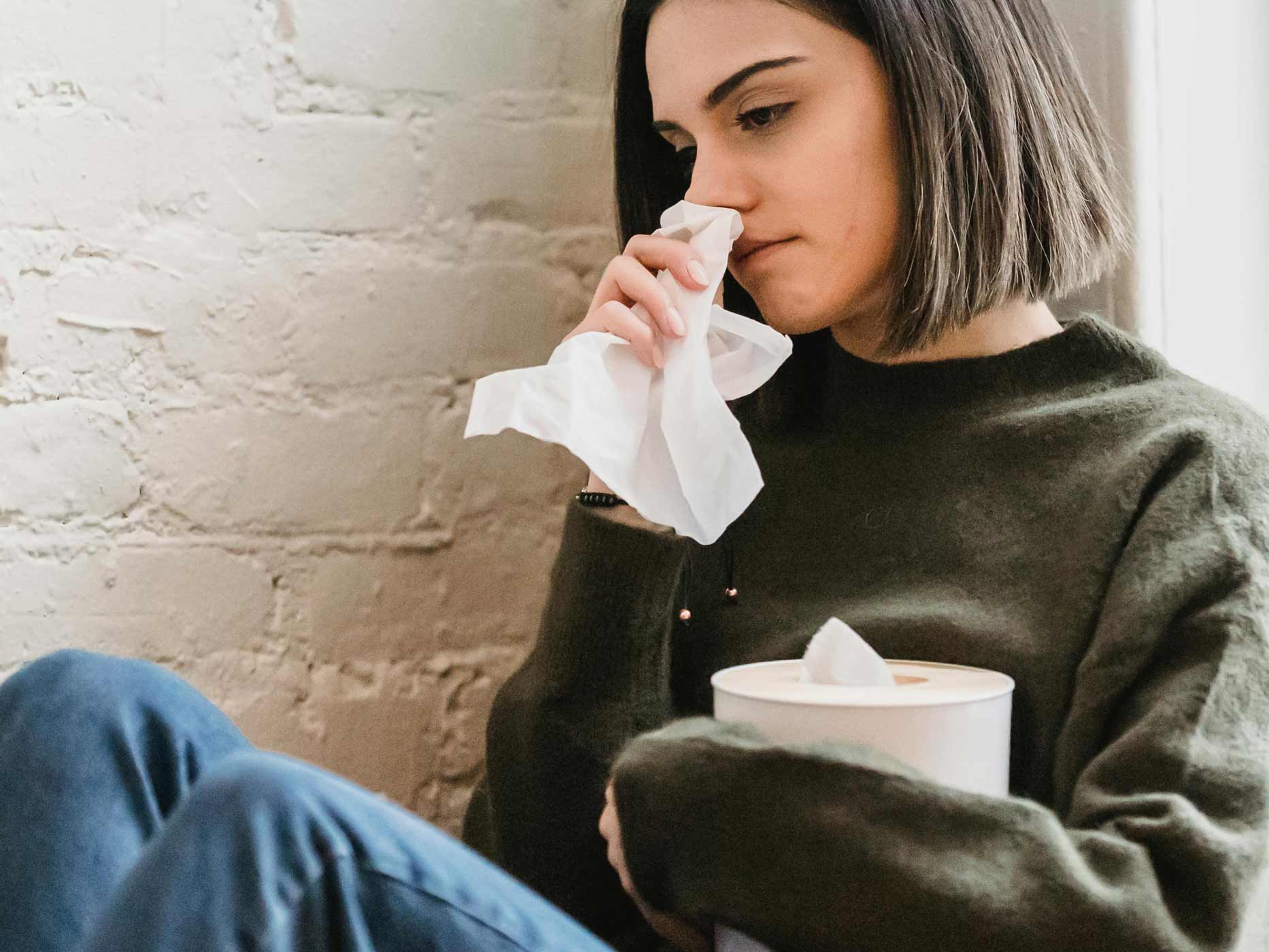 Liebeskummer loswerden Tipps Ein Mädchen sitzt an einer Wand, hält sich ein Taschentuch an die Nase und weint.