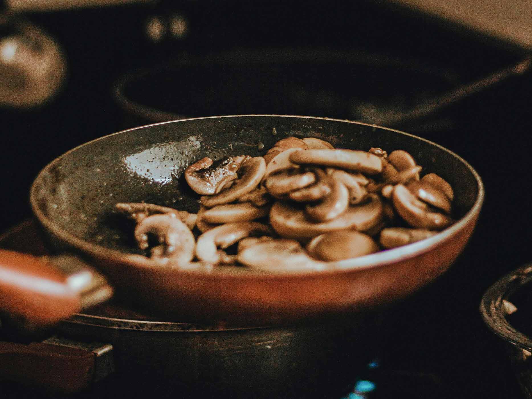 Herbst herzhafte Pilzgerichte Eine Pfanne steht auf dem Herd. In ihr werden Pilze gebraten.