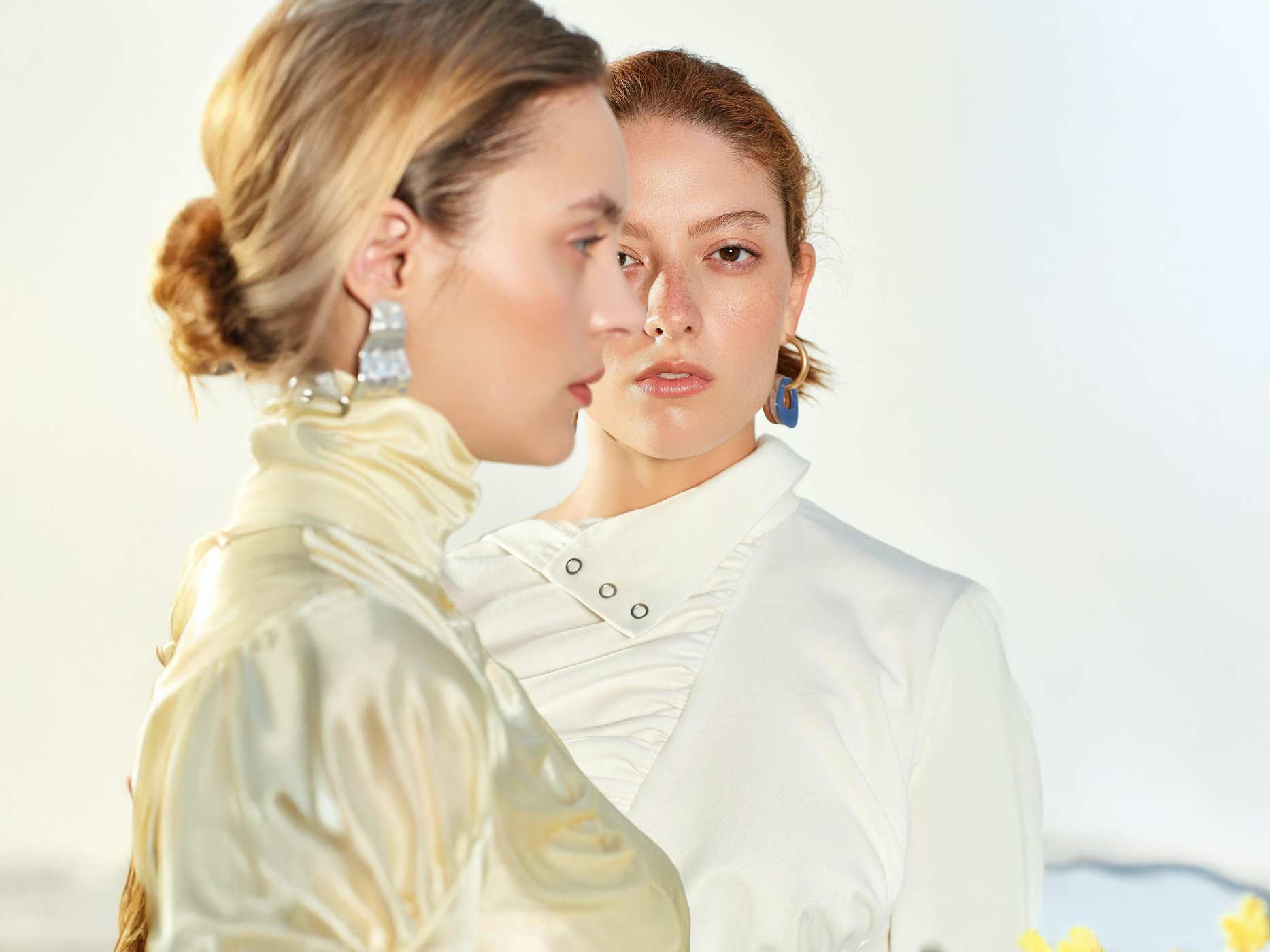 Laufstegtrends in Alltagsmode Zwei Frauen schauen in unterschiedliche Richtungen. Sie tragen beide elegante Kleidung in Weiß und Cremefarben.