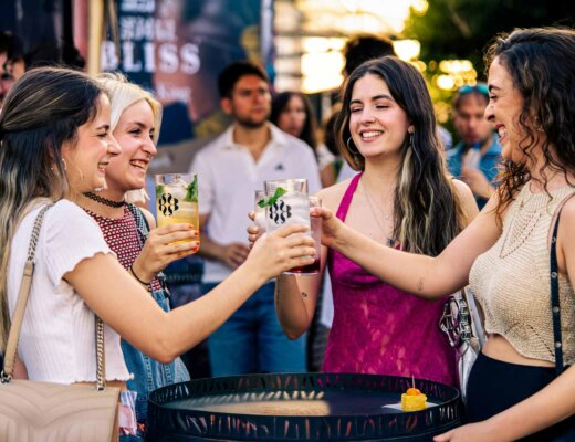 Vier Frauen stehen um einen Tisch rum und stoßen mit ihren Getränken an.