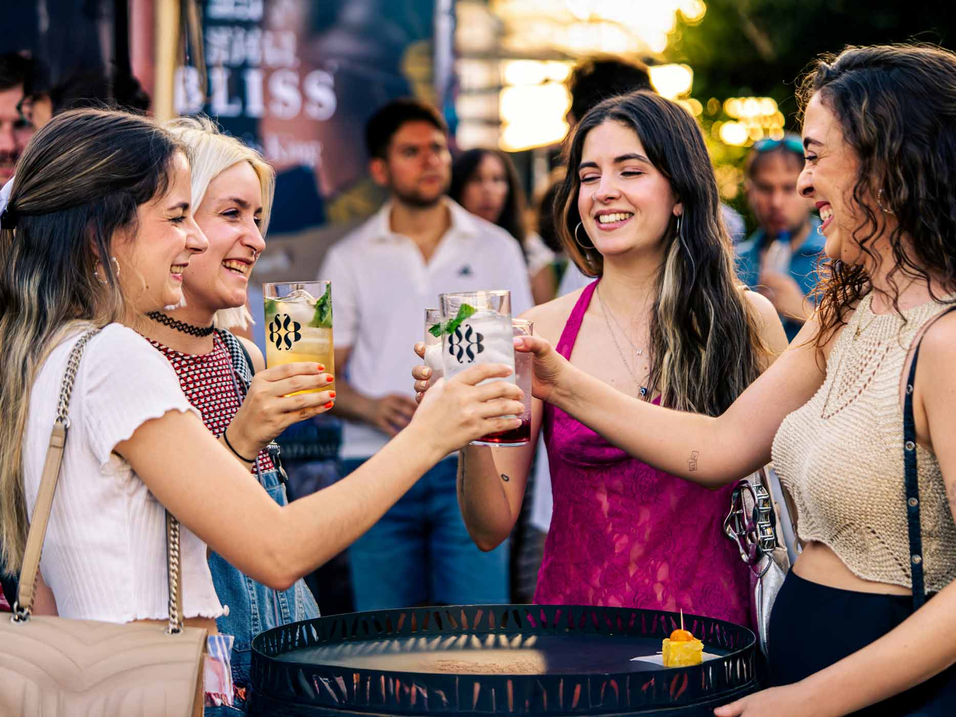 Passendes Outfit Anlass Vier Frauen stehen um einen Tisch rum und stoßen mit ihren Getränken an.