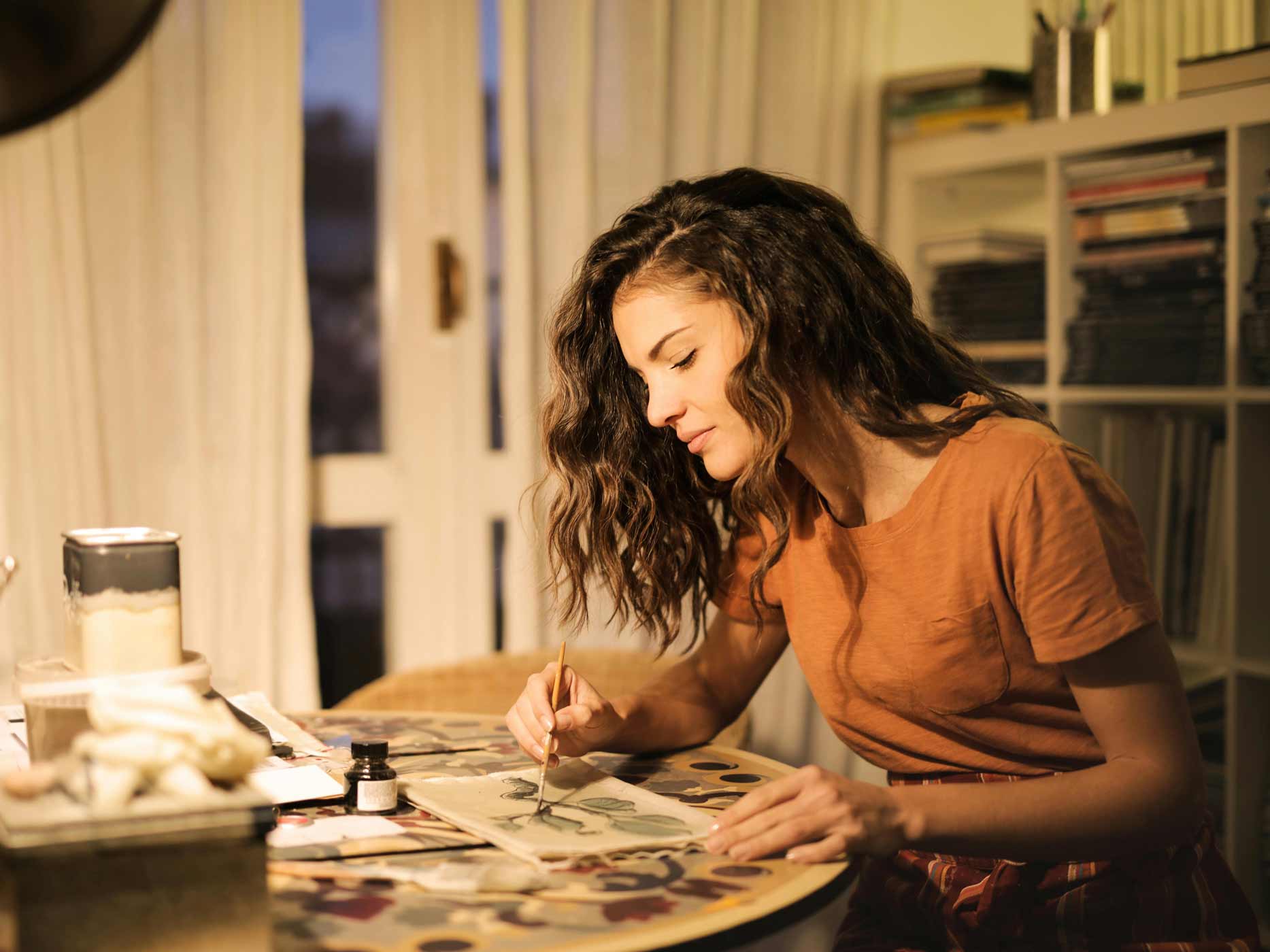 Verregnete Wochenenden Hobby Eine Frau sitzt am Tisch und malt mit einem Pinsel etwas auf ein Blatt.