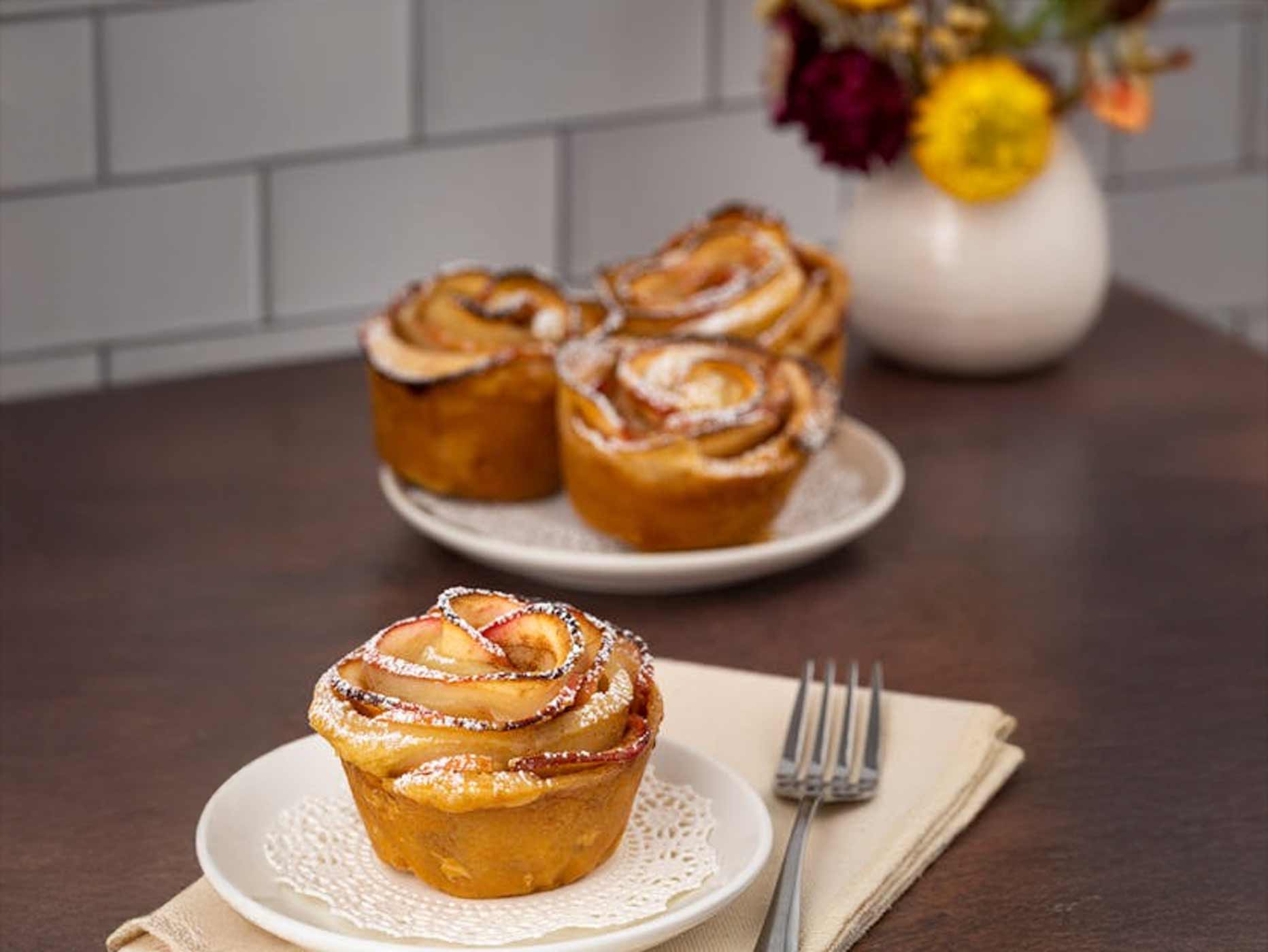 Geburtstag Essensideen Mit Puderzucker bestäubte Apfelrosen stehen auf zwei Tellern verteilt auf einem Tisch.