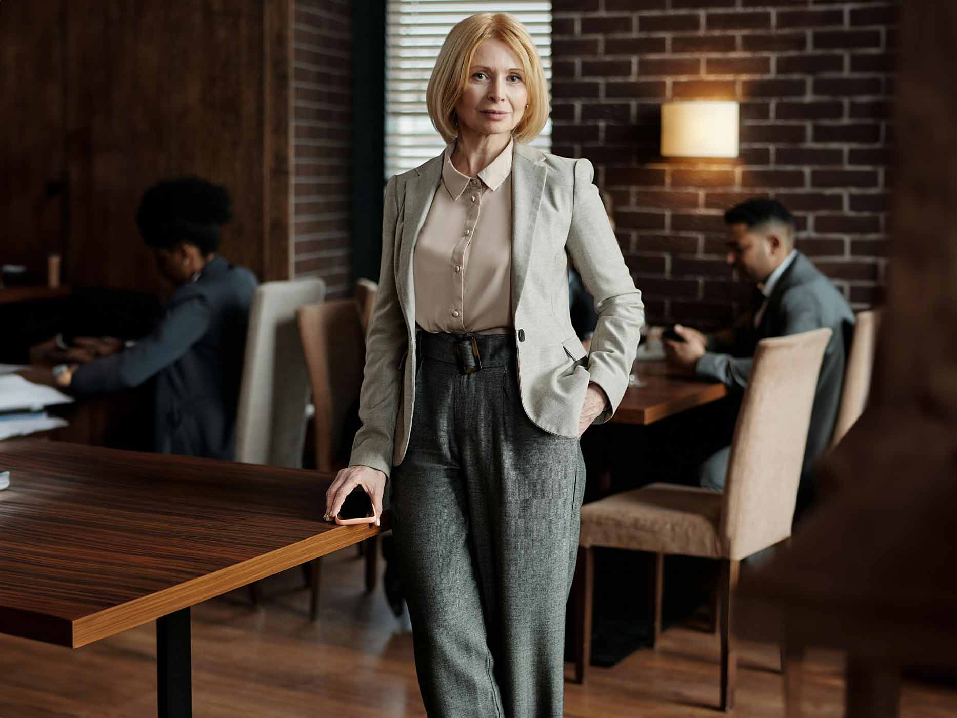 Frau trägt beige Bluse, darüber einen hellgrauen Blazer und eine dunkelgraue Schlaghose als Büro-Outfit