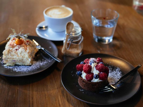 Verschiedene Desserts stehen auf Tellern auf einem Tisch, daneben stehen eine Tasse Kaffee und ein Glas Wasser.