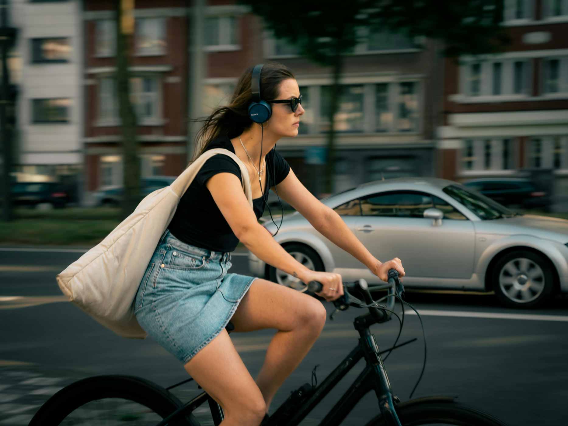 Frau fährt Fahrrad und trägt eine große, weiße Umhängetasche über der Schulter