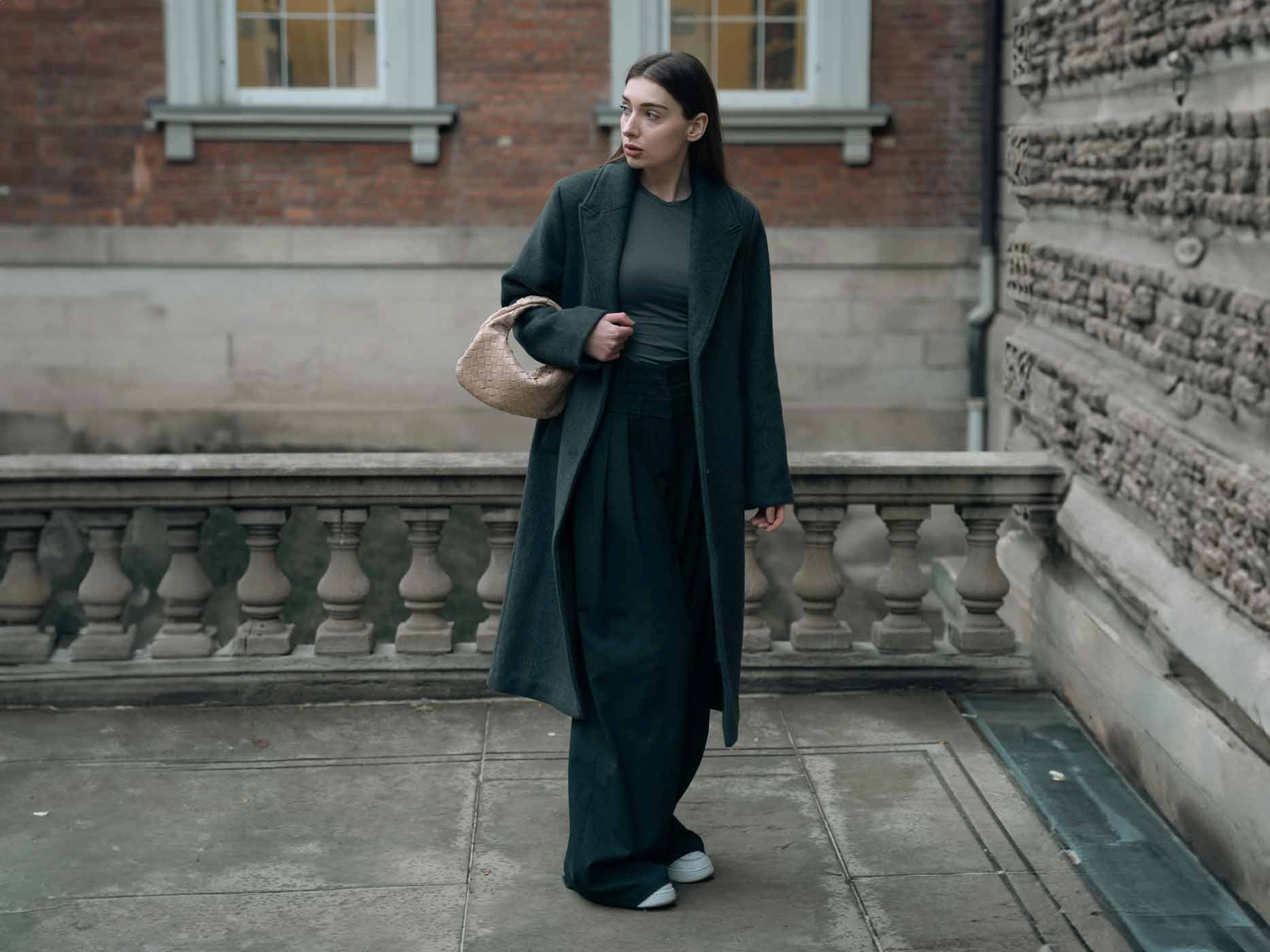 Frau trägt dunkle Schlaghose zu weitem, dunklem Oberteil und Mantel