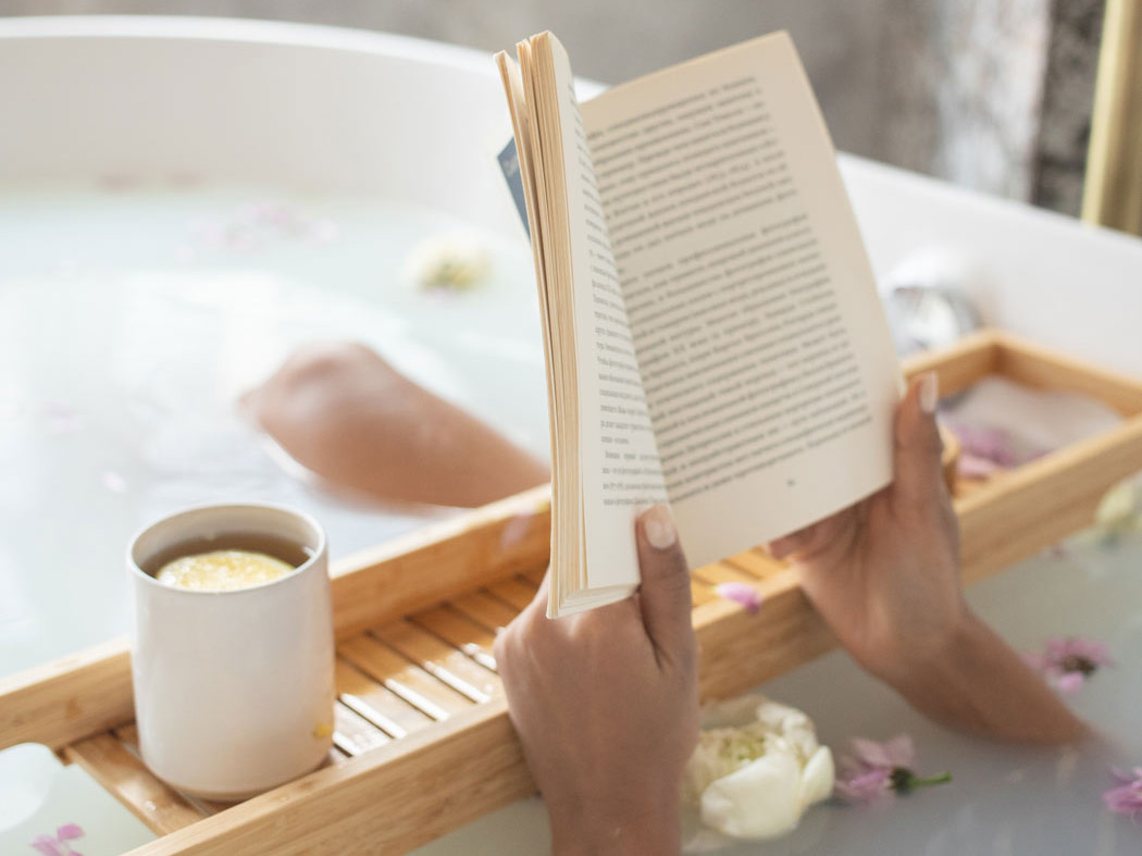 Frau in der Badewanne, die ein Buch liest und einen Kaffee auf der Ablage hat.