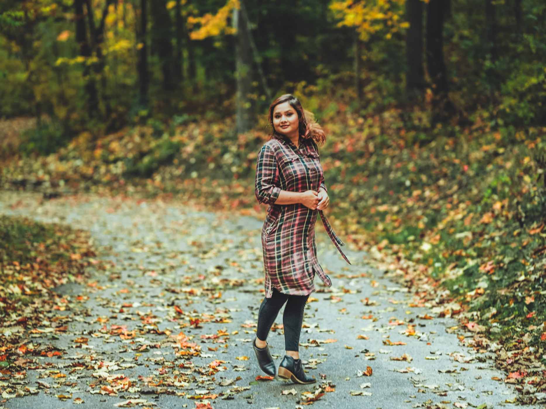 Frau steht vor Herbstwald und trägt ein rot-grün kariertes Hemdkleid mit Stiefeln und dreht sich dabei