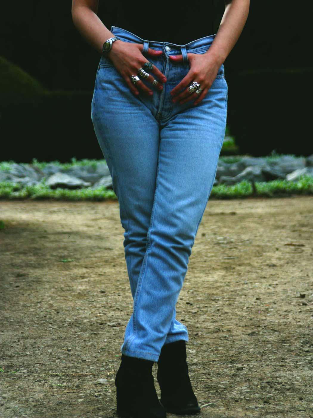Frau in Slim Fit Jeans, die mit gekreuzten Beinen und Händen in den Gürtelschlaufen steht.