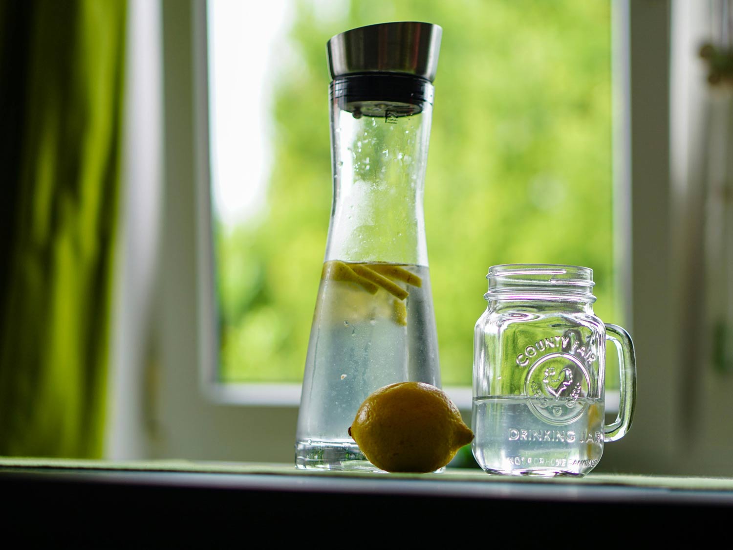 Gefüllte Wasserkaraffe mit Zitronenscheiben, daneben steht ein Glas.