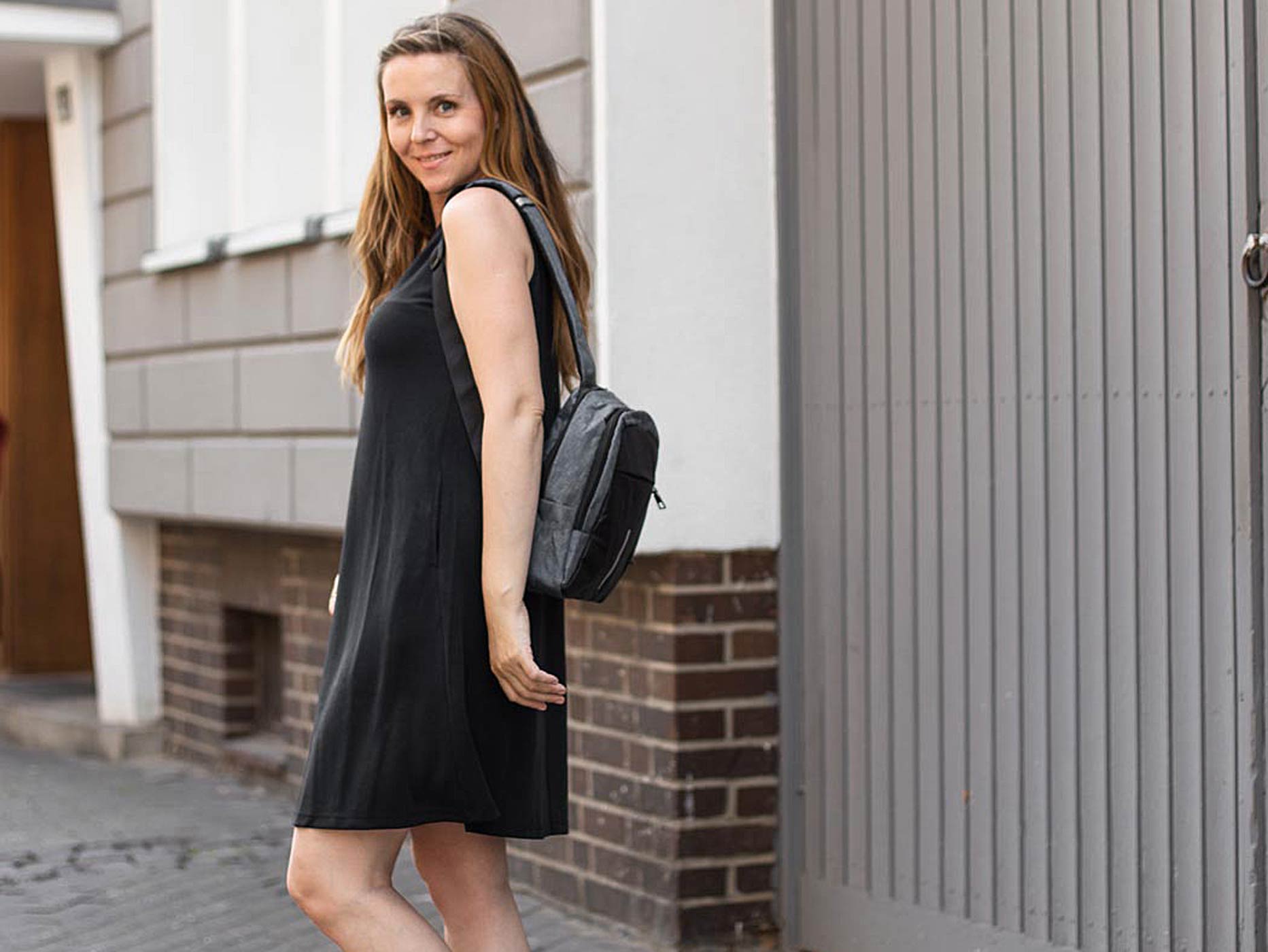 Frau trägt leichtes, schwarzes Sommerkleid und einen kleinen schwarzen Rucksack