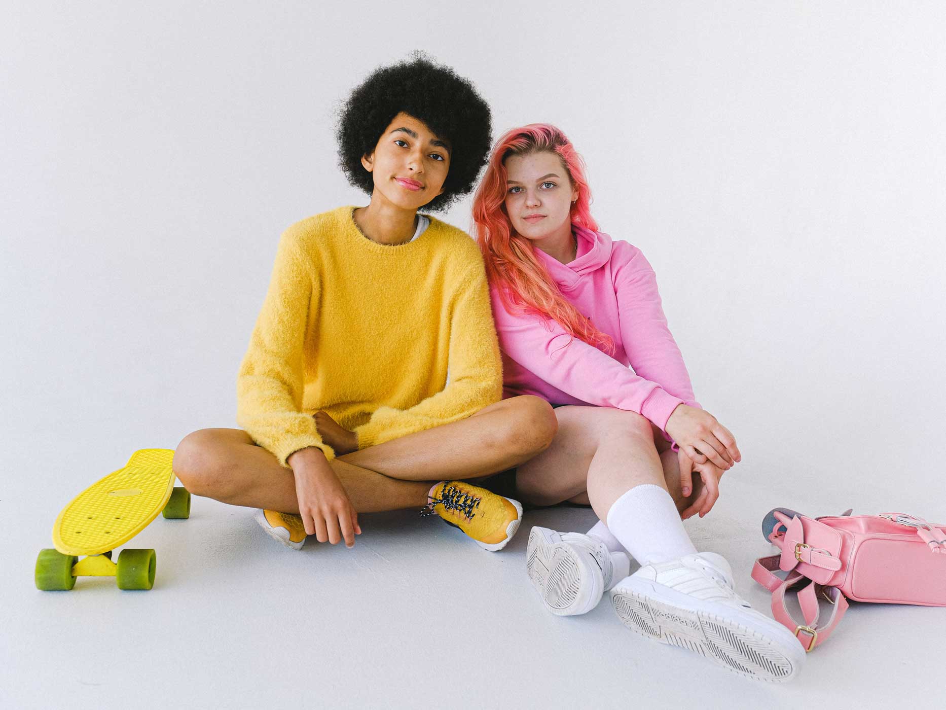 Zwei Mädchen sitzen vor einem neutralen Hintergrund, die eine trägt ein komplett gelbes Outfit, die andere ist nur in Pink gekleidet