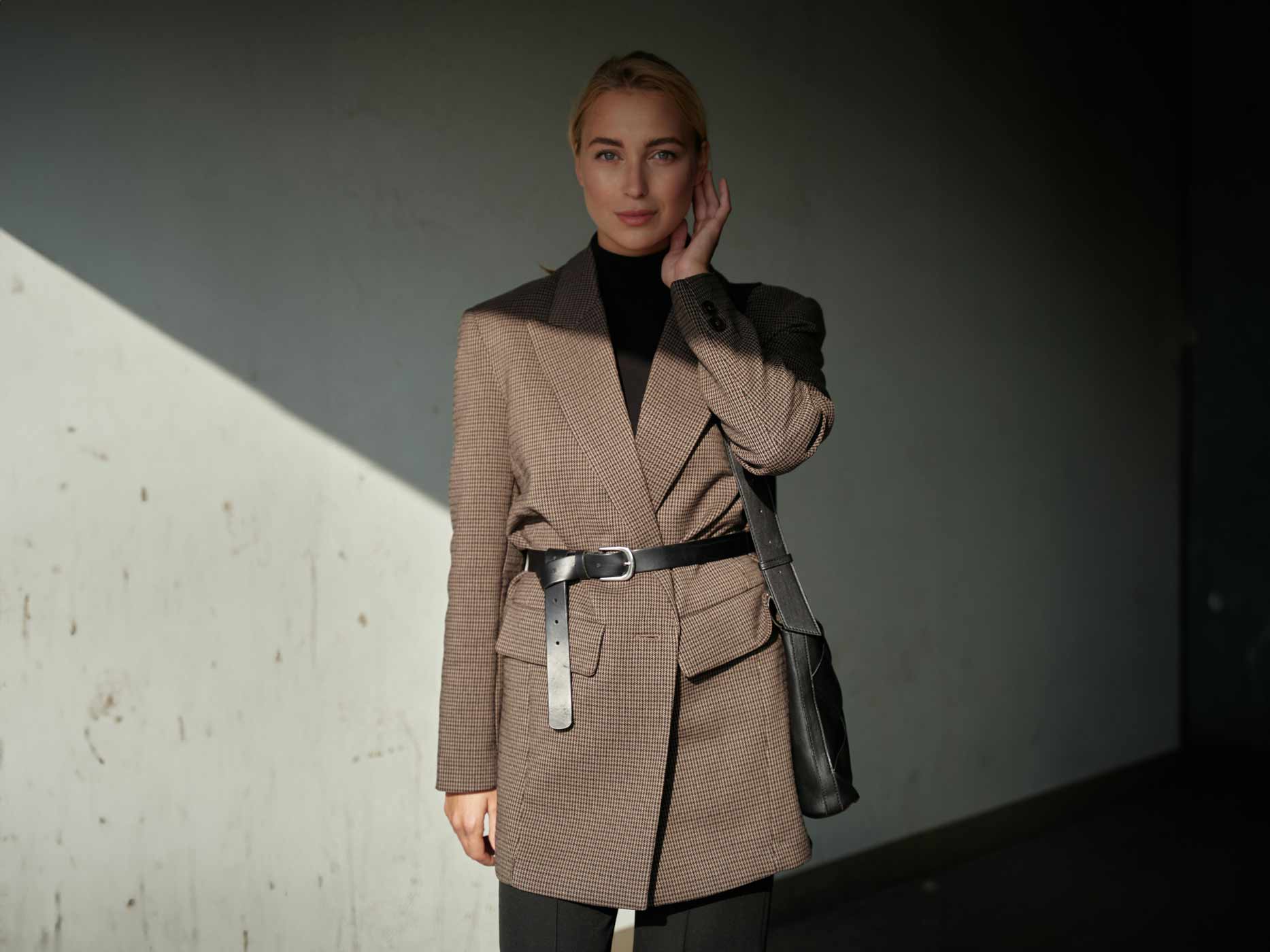Frau trägt schwarzen Rollkragenpullover mit kariertem Blazer, den ein Gürtel geschlossen hält