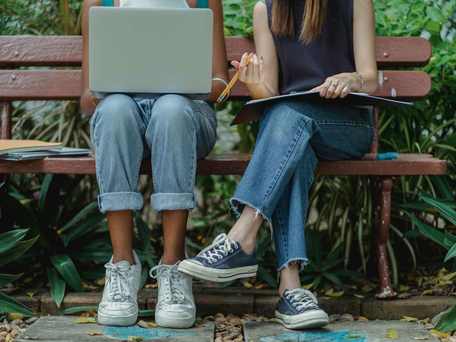 Zwei Frauen sitzen auf einer Bank und tragen Jeans, die die Knöchel zeigen