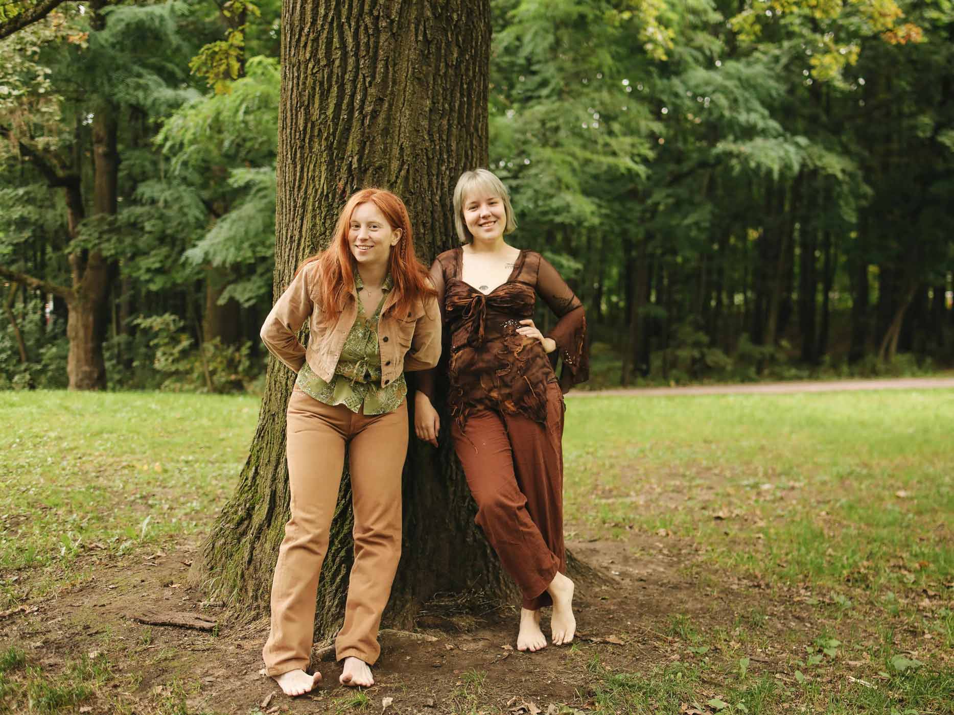 Zwei Frauen lehnen sich an einen Baum und tragen Kleidung in Erdtönen