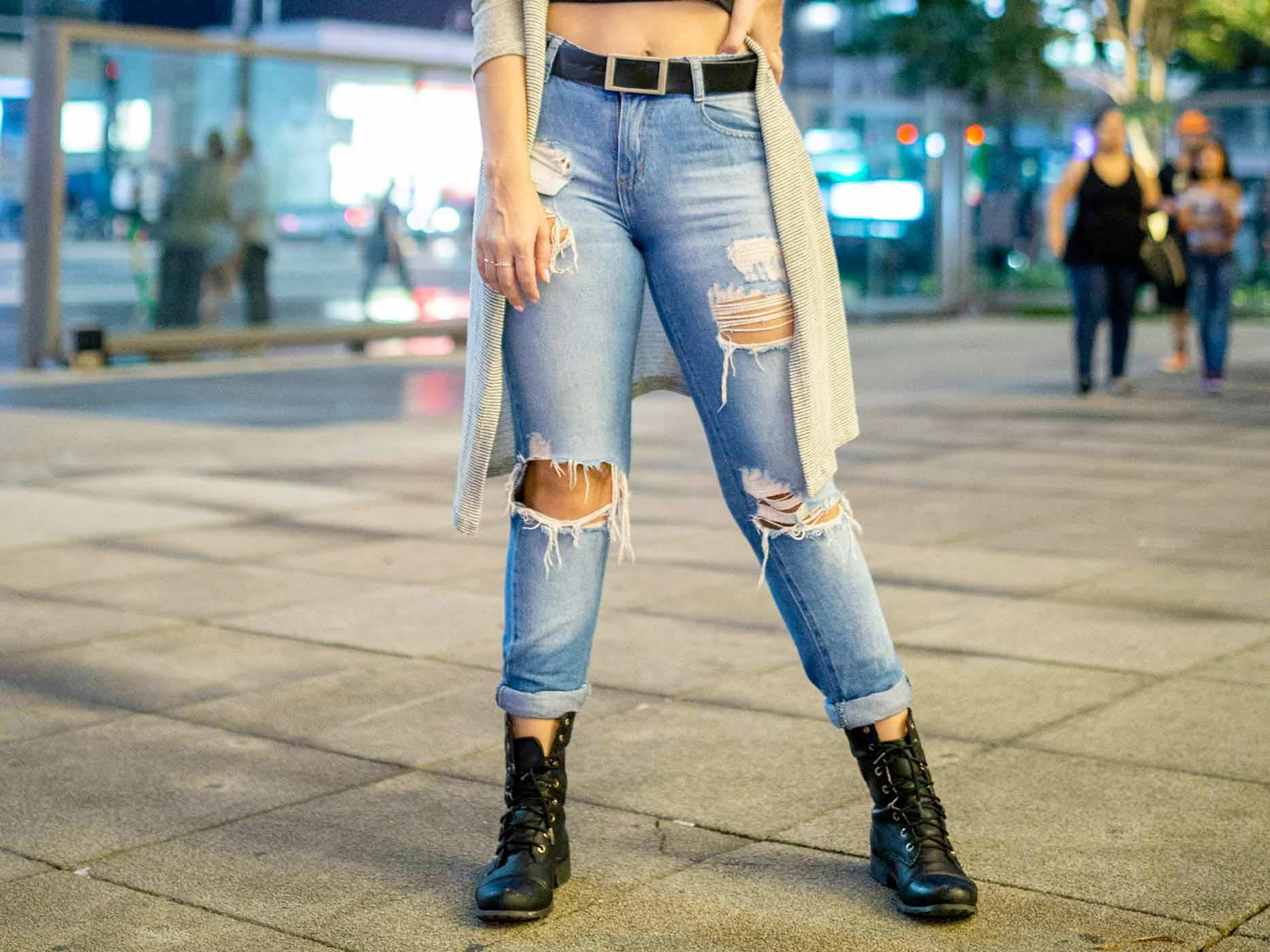 Frau in blauer Ripped Jeans mit Gürtel und Boots