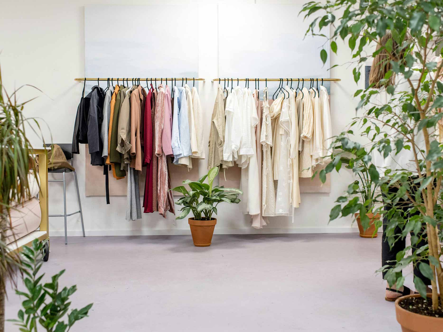 Klamotten hängen mitten in einem Raum voller Pflanzen geordnet auf Kleiderstangen