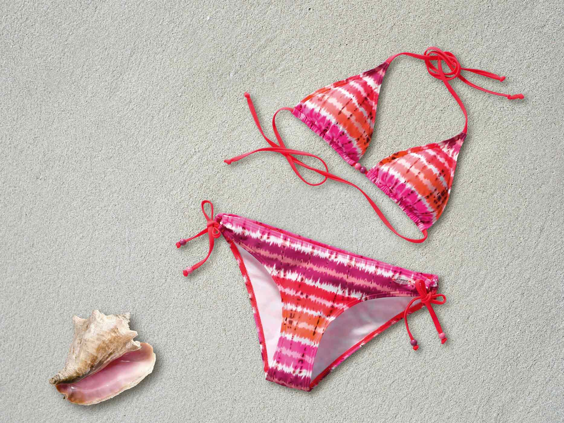Ein orange-pink gemusterter Bikini liegt ausgebreitet am Strand