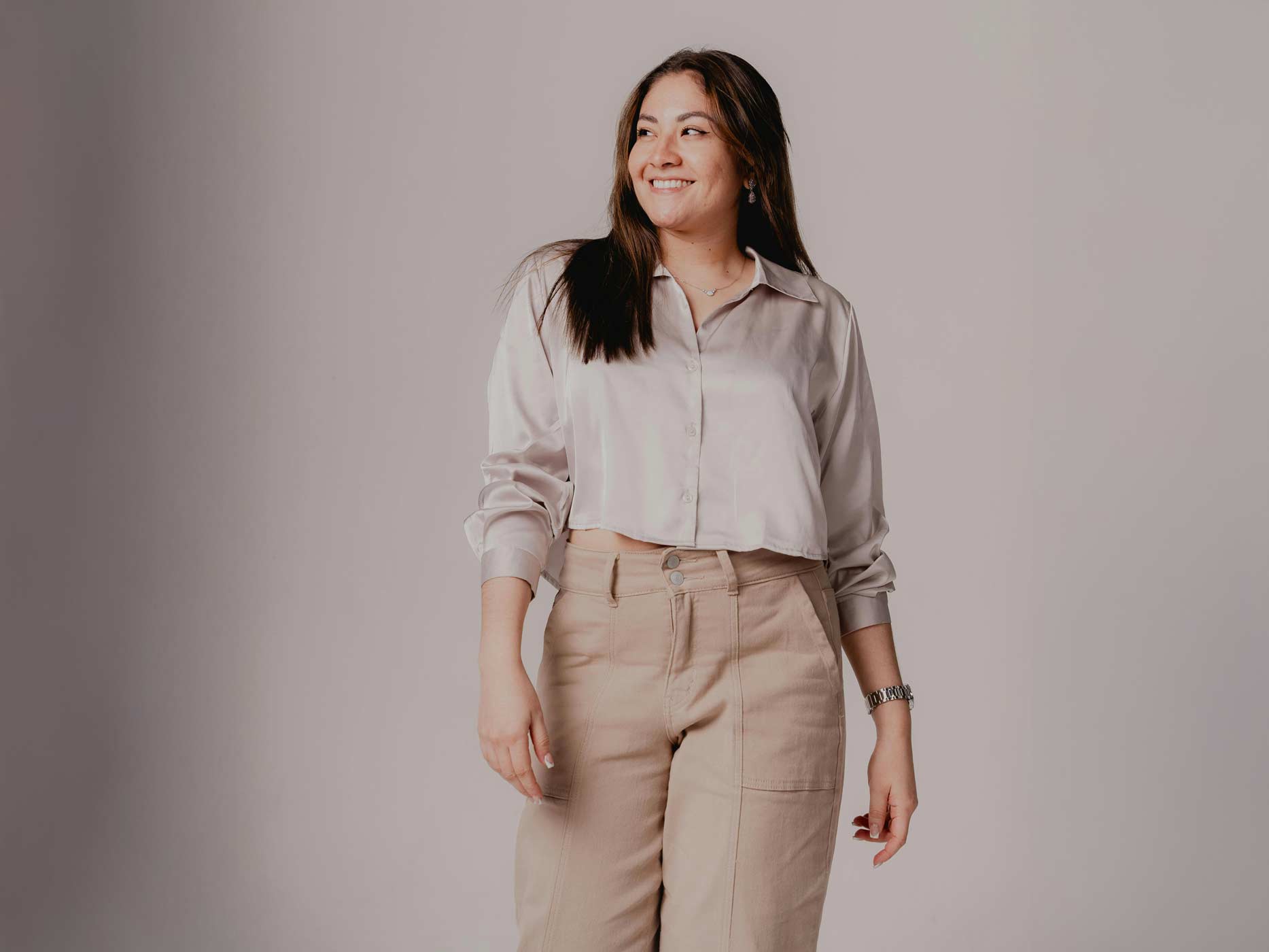 Eine Frau trägt eine beige Highwaist Stoffhose und ein gecropptes, beiges Hemd.