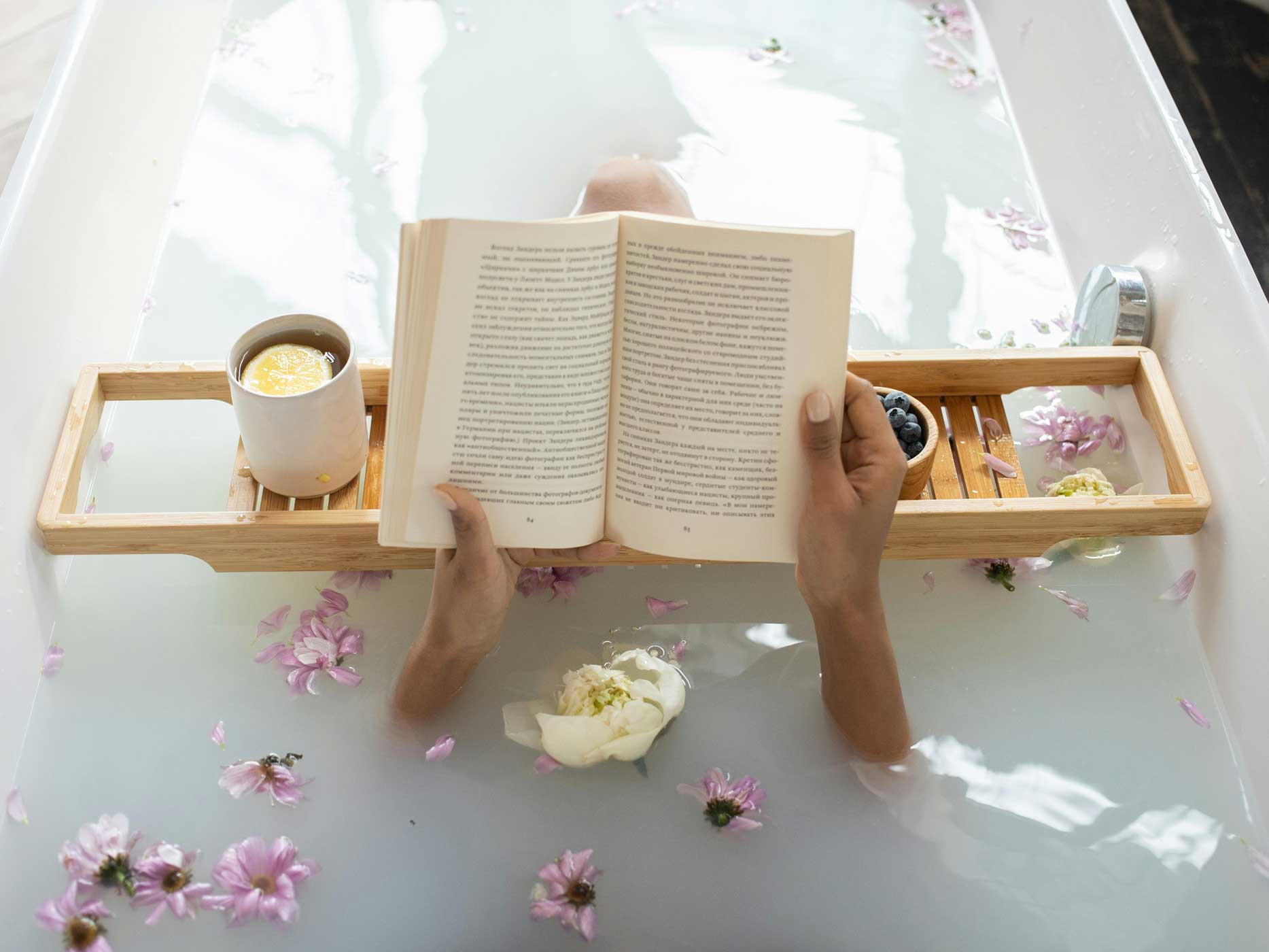 Frau liegt mit Blumen im Wasser in der Badewanne und liest ein Buch