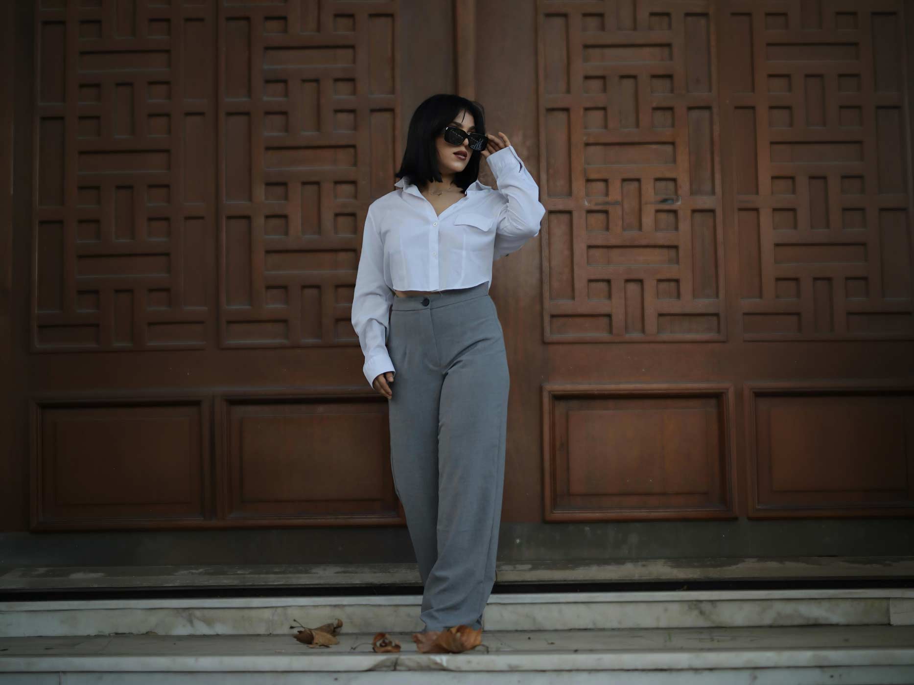 Eine Frau tr&auml;gt eine graue Stoffhose und dazu eine kurze wei&szlig;e Bluse.